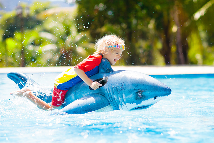A boy has fun in a pool with an inflatable shark.