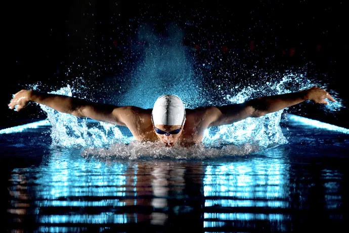 Front view of a butterfly swimmer recovering his arms forward above the water.
