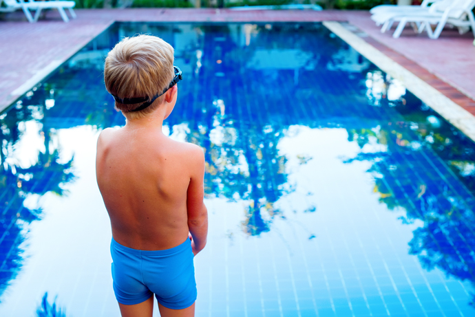 A young boy experiencing fear of swimming while standing in front of a pool