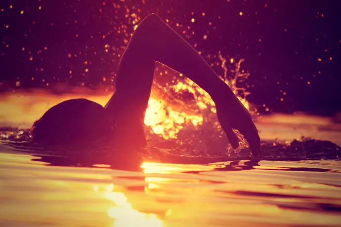 A front crawl swimmer swimming with a sunset in the background