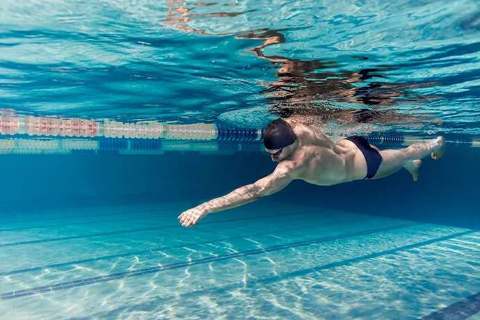 A young male front crawl swimmer is engaging his core muscles to swim with more power.