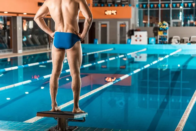 A swimmer in swimming trunks standing on a starting block