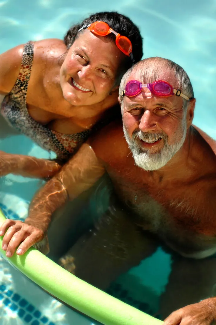 A happy elderly couple is relaxing in an outdoor pool on a sunny day.